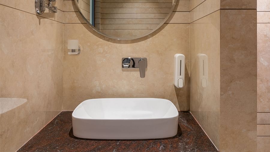 A bathroom features a round wall-mounted mirror above a wash basin | Hotel Ganga Maiya
