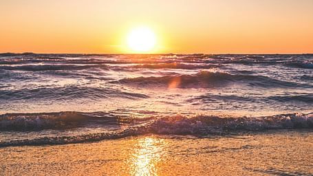 A vibrant sunset casts a golden glow across a sandy beach and the ocean waves.