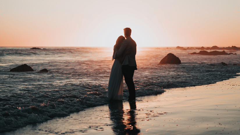 A couple stares at the sunset on a beach one of the best Valentine s Weekend Getaways.