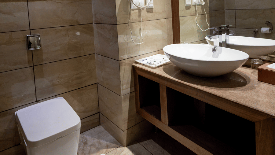 A bathroom with a sink, mirror, toilet, and shower area with tiled walls at Indraprastha Resort & Spa, McLeod Ganj.
