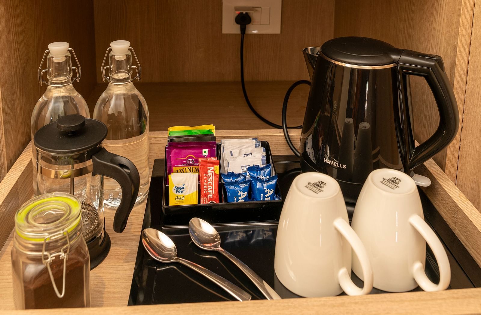 Wooden cabinet with a safe, kettle, and tableware at Nivasana Manali.