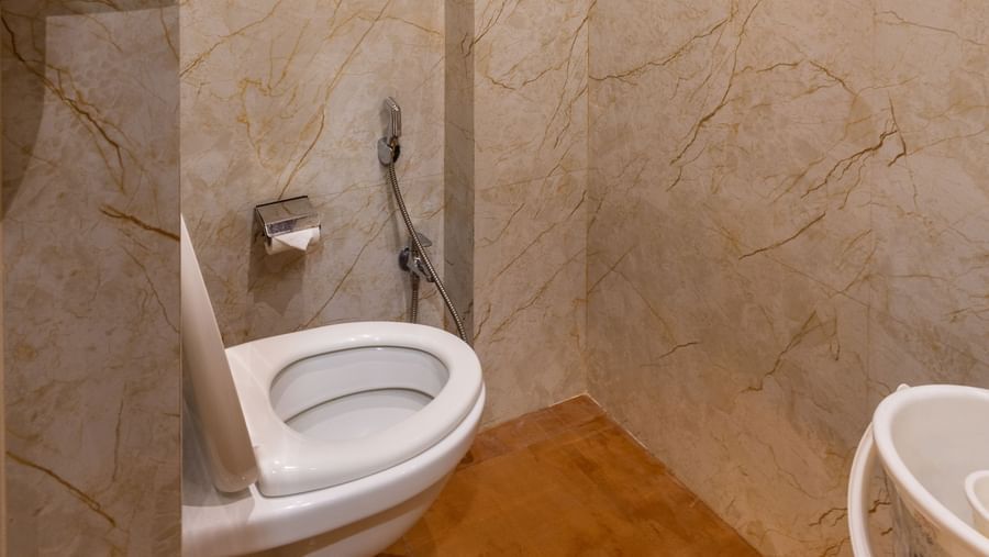 Bathroom with beige tiled walls, shower, geyser, and toilet at Pravasa Stay Dewas Naka, Indore.
