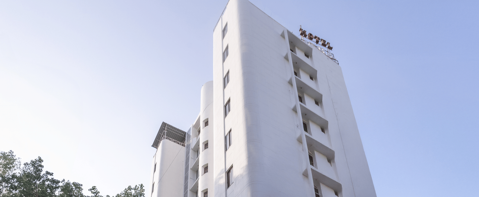 Exterior view of the tall, white hotel building standing against a clear sky, with a driveway leading to the entrance at Pravasa Stay, Vadodara.