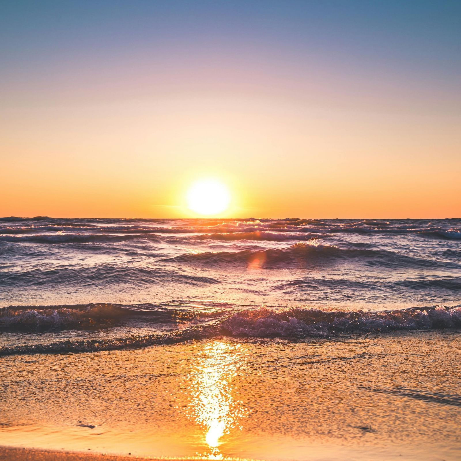Sunrise at the beach, waves gently lapping the shore, with the sun reflection dancing on the water beneath a clear sky