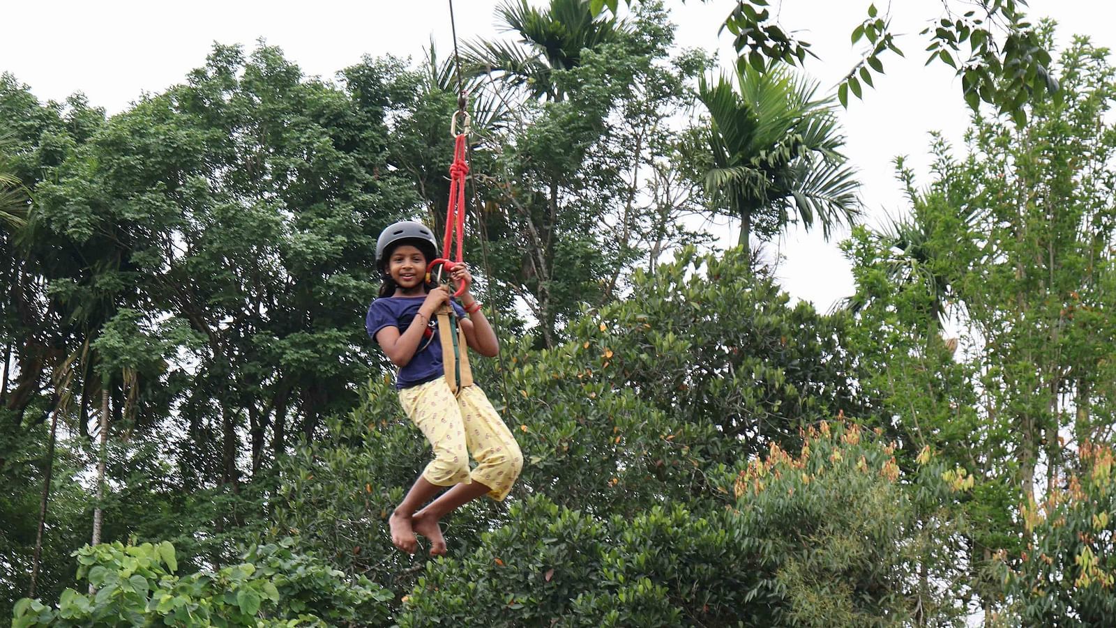Image of a girl doing zip lining at the play area of our hotel | Great Trails Wayanad by  GRT hotels.