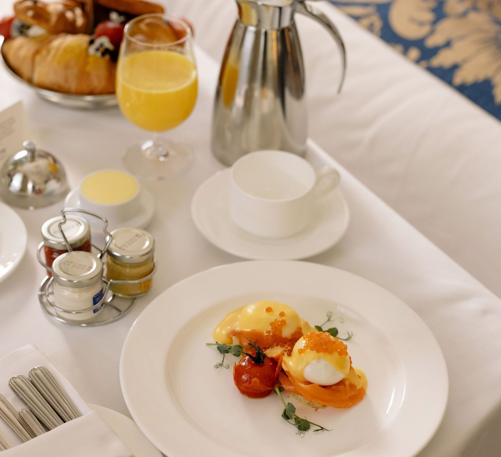 A hotel breakfast with eggs benedict, pastries and orange juice on a table