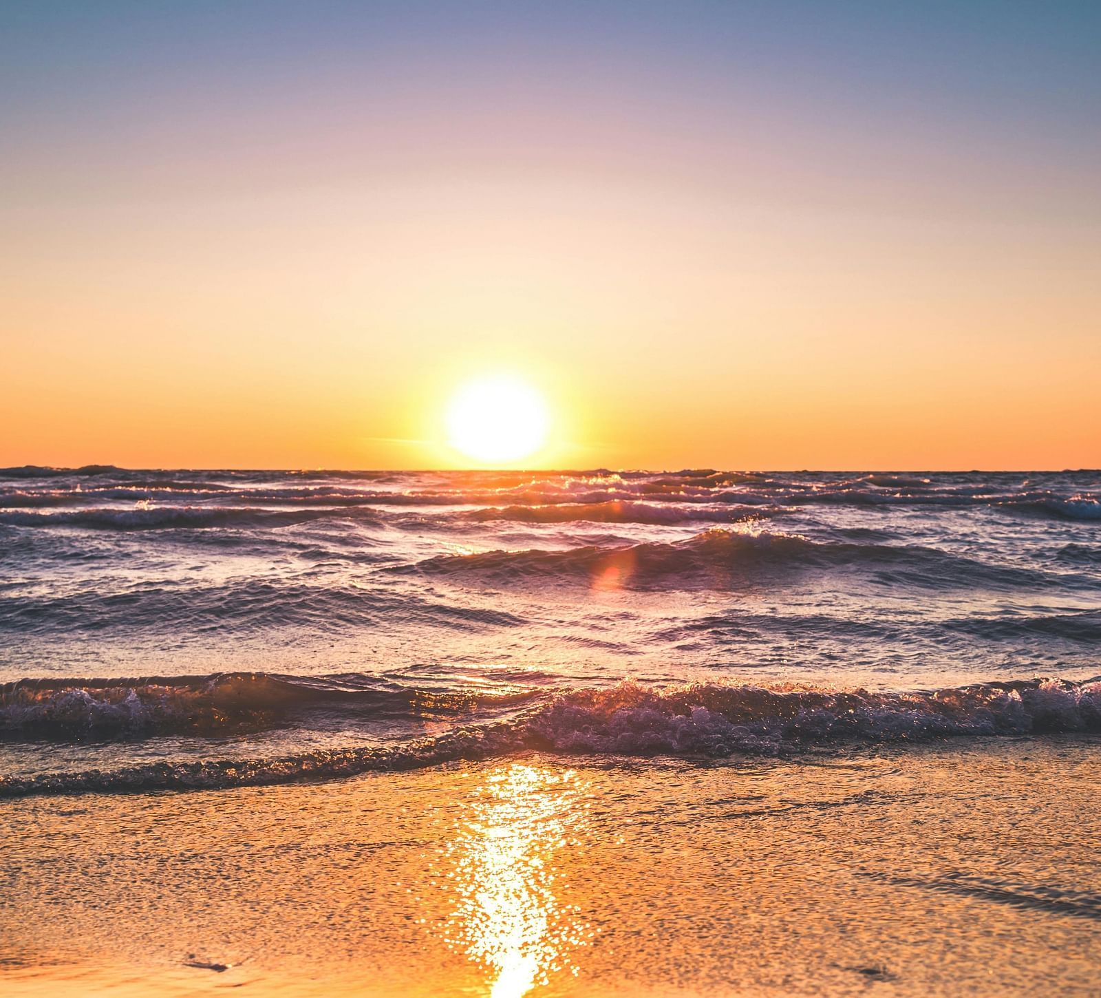 Sunrise at the beach, waves gently lapping the shore, with the sun reflection on the water beneath a clear sky
