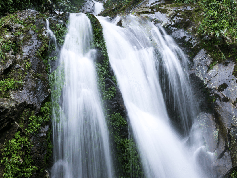 A waterfall surrounded by lush green forest and rocks.