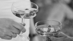 A gray image of a couple holding glasses together.