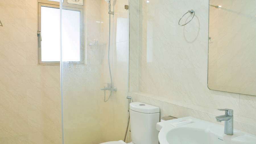 A clean, compact bathroom featuring a white toilet, a ceramic pedestal sink, and a glass-enclosed walk-in shower area at Apartel by Aarin, Oragadam.