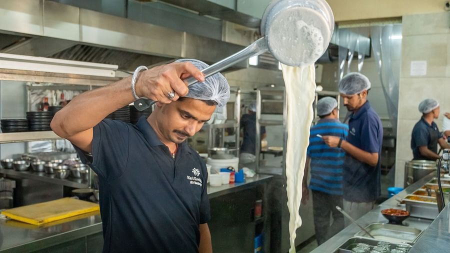 A person standing beside the kitchen counter at Hari Govinda's, pouring milk into a container