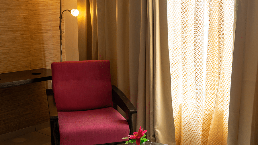 A small seating area with a glass-top table and a armchair next to a window with golden curtains - Hotel Udai Median, Udaipur.