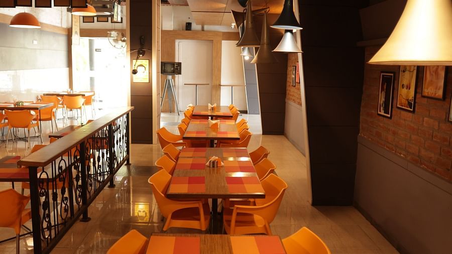a long wooden dining area with orange coloured cushioned chairs arranged around it - Max Hotel, Jabalpur