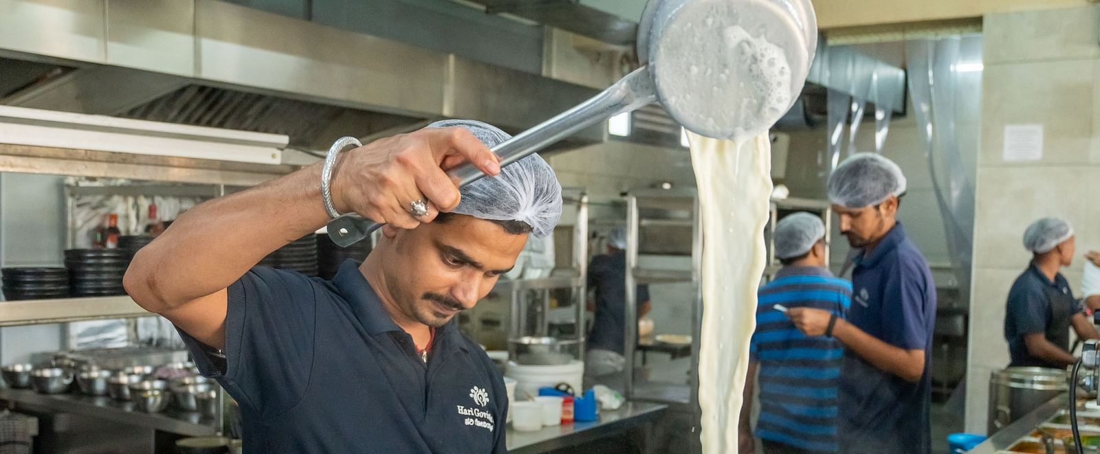 A person standing beside the kitchen counter at Hari Govinda's, pouring milk into a container