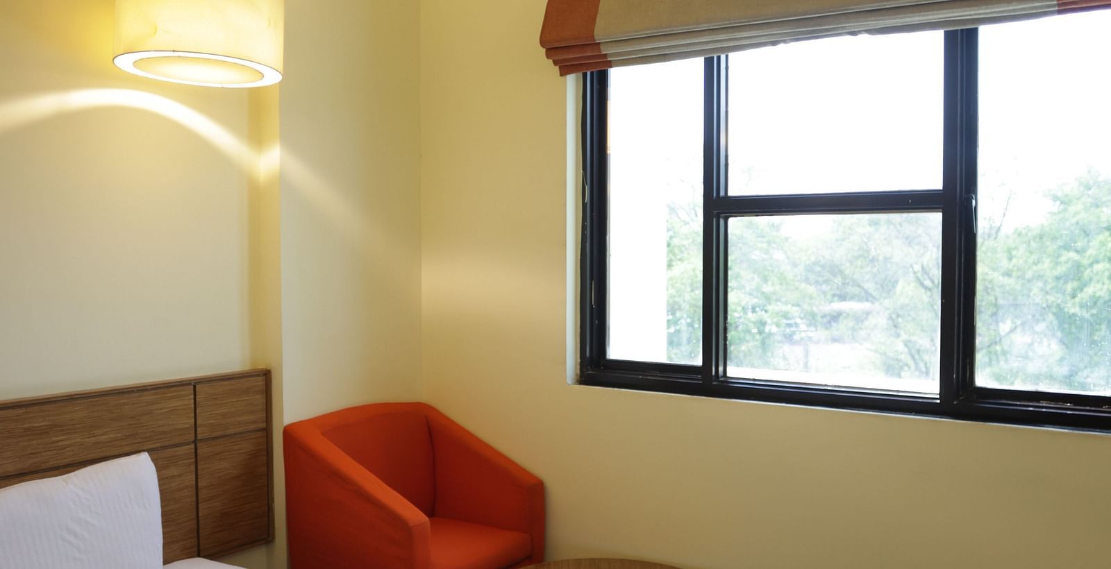 a close up shot of a comfortable single bed with a red cushioned armchair in the corner of the room with a coffee table in front of it  - Max Hotel Jabalpur