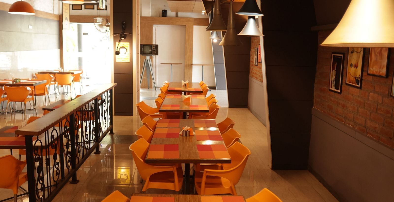 a long wooden dining area with orange coloured cushioned chairs arranged around it - Max Hotel, Jabalpur