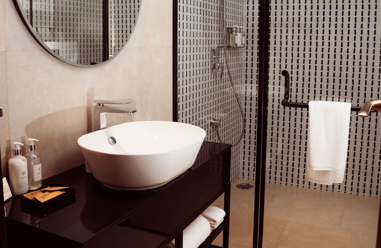 Washroom with a large washbasin beneath a round mirror and a glass door separating the shower area at Nivasana Manali.