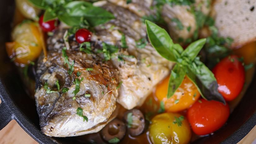 An image baked fish on a pan with a colourful assortment of vegetables.