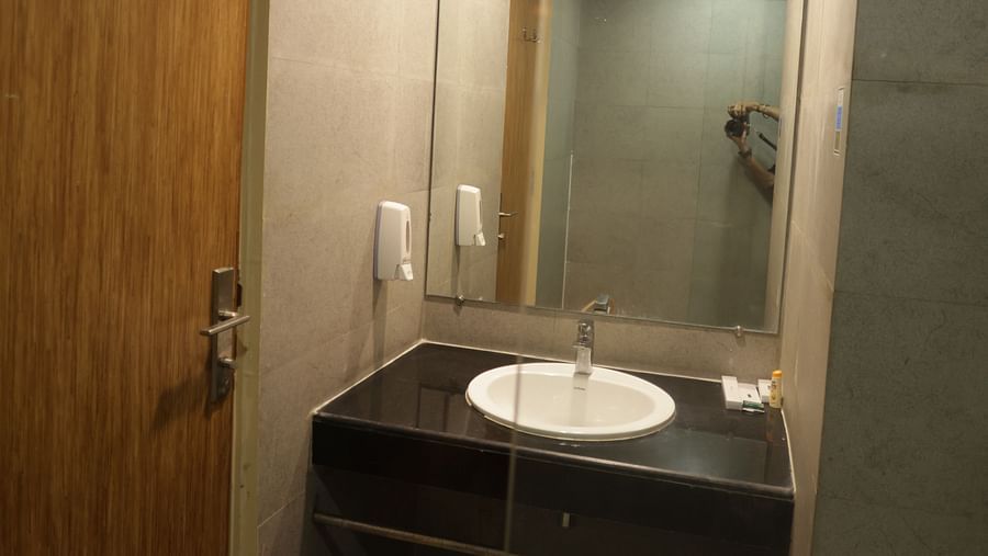 a washbasin with a black counter top and a wide mirror above it - Max Hotel Jabalpur
