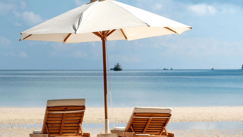 image of a beach featuring two sun loungers shaded with a white umbrella