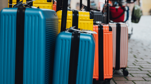 A row of colorful travel suitcases stands parked outdoors on a paved walkway.