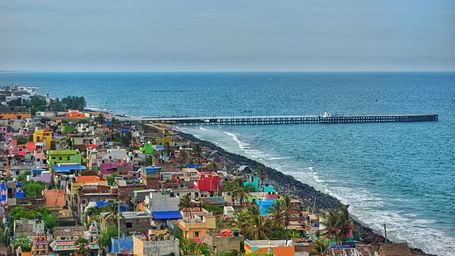 An aerial view of Pondicherry featuring colourful buildings clustered along the coastline next to the Bay of Bengal and a long pier extending into the sea.