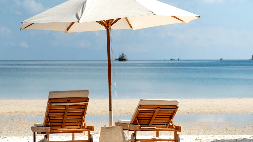 image of a beach featuring two sun loungers shaded with a white umbrella