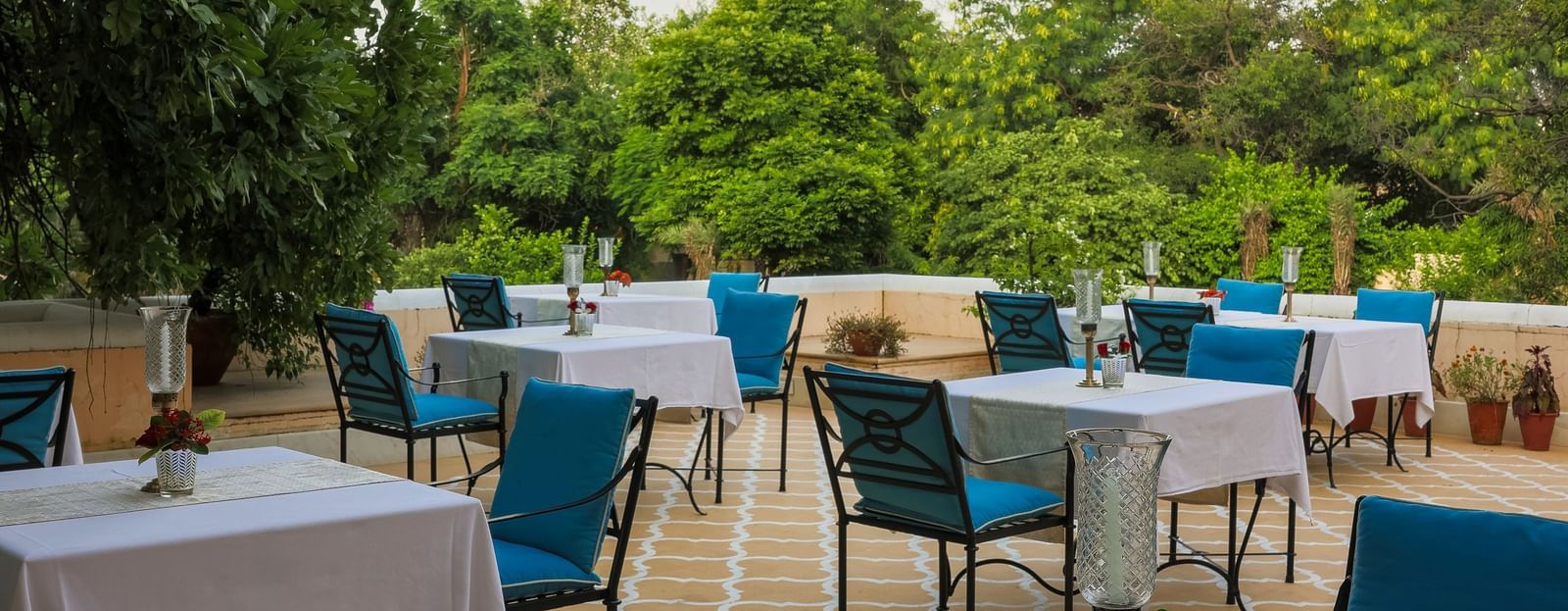 Outdoor tables and chairs set up on a patio or lawn at Royal Heritage Haveli under a blue sky with some trees.