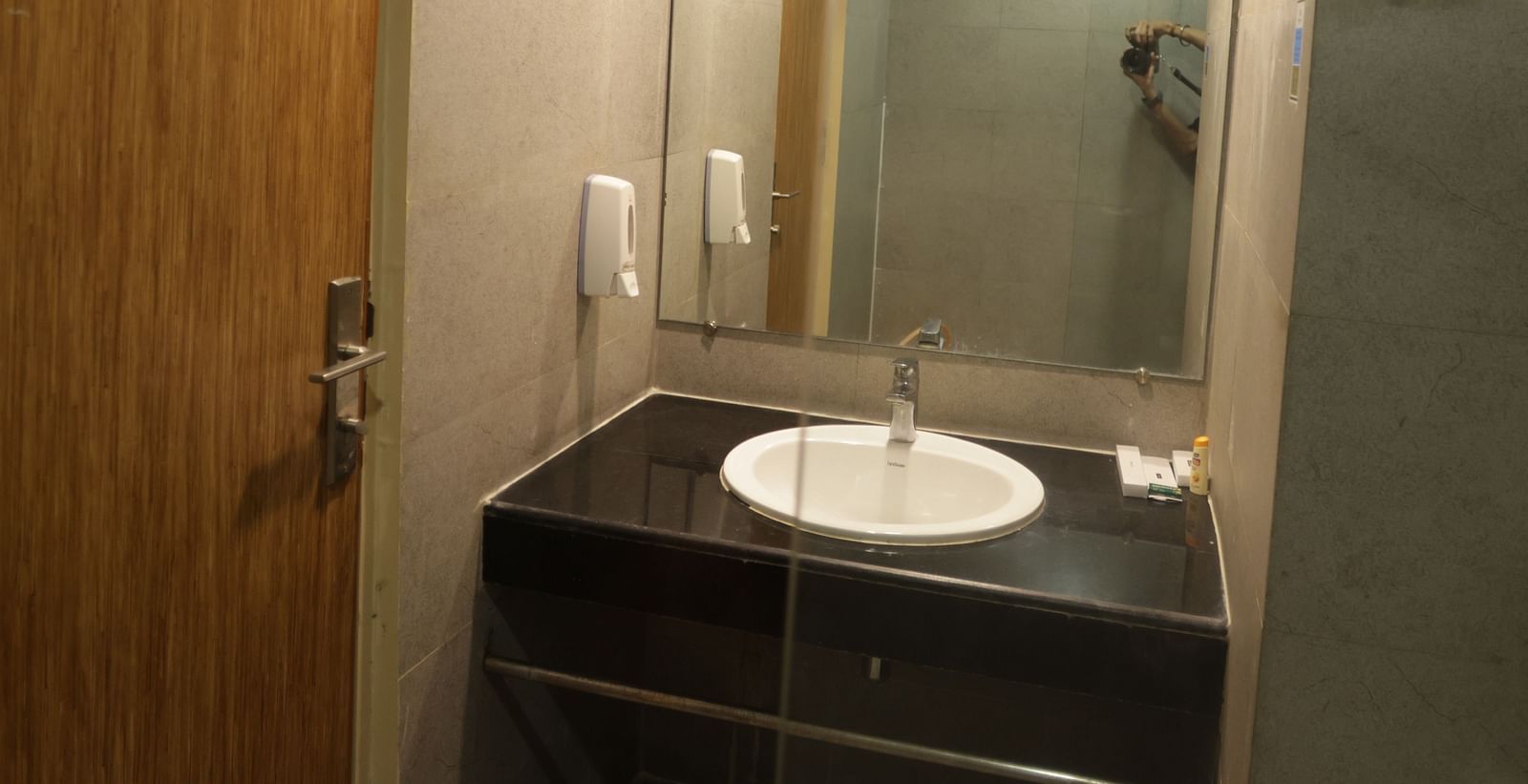 a washbasin with a black counter top and a wide mirror above it - Max Hotel Jabalpur