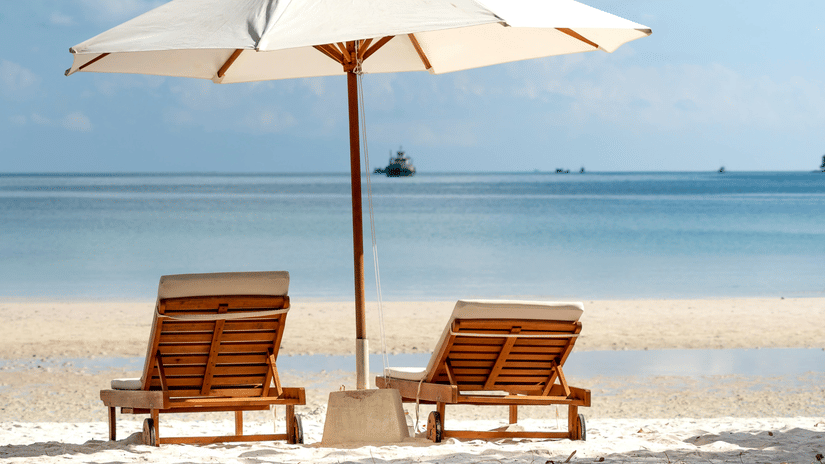 image of a beach featuring two sun loungers shaded with a white umbrella