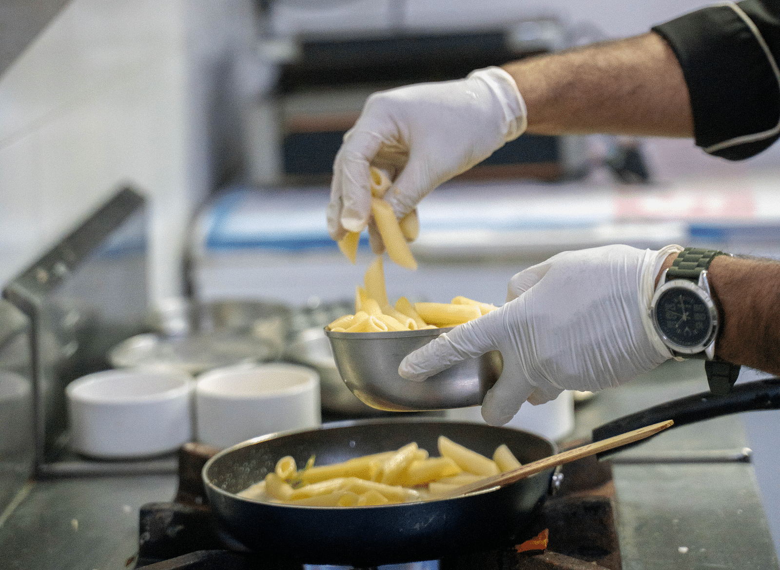 A chef adding boiled pasta to a pan over a stove | Hotel Udai Median, Udaipur