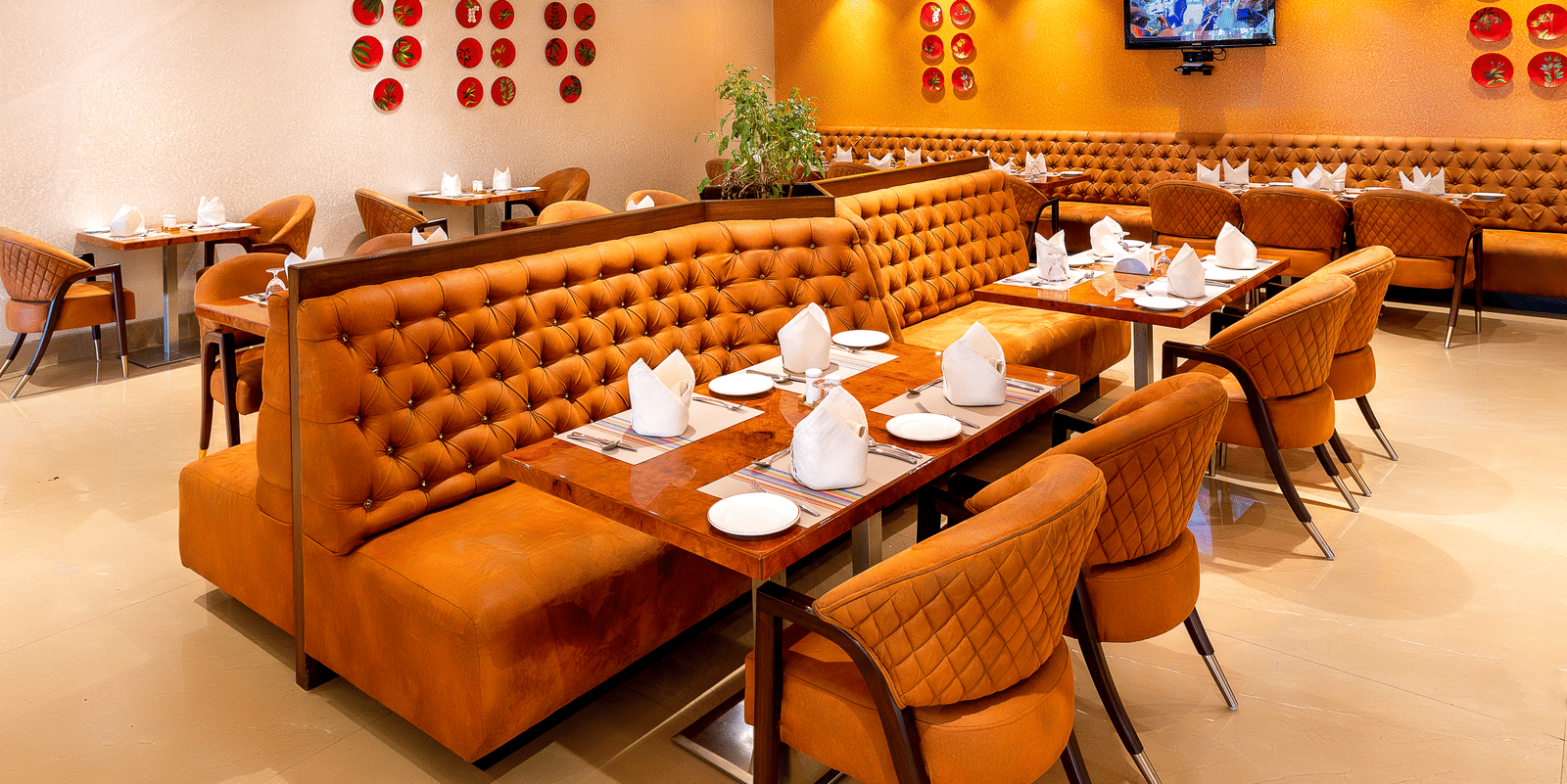 Interior view of the brightly lit restaurant showing the corner seating, orange booths, and large decorative glass ceiling at Hotel Hukam's Lalit Mahal.