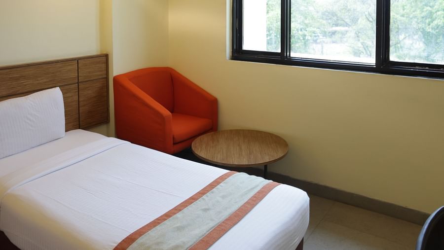 a close up shot of a comfortable single bed with a red cushioned armchair in the corner of the room with a coffee table in front of it  - Max Hotel Jabalpur