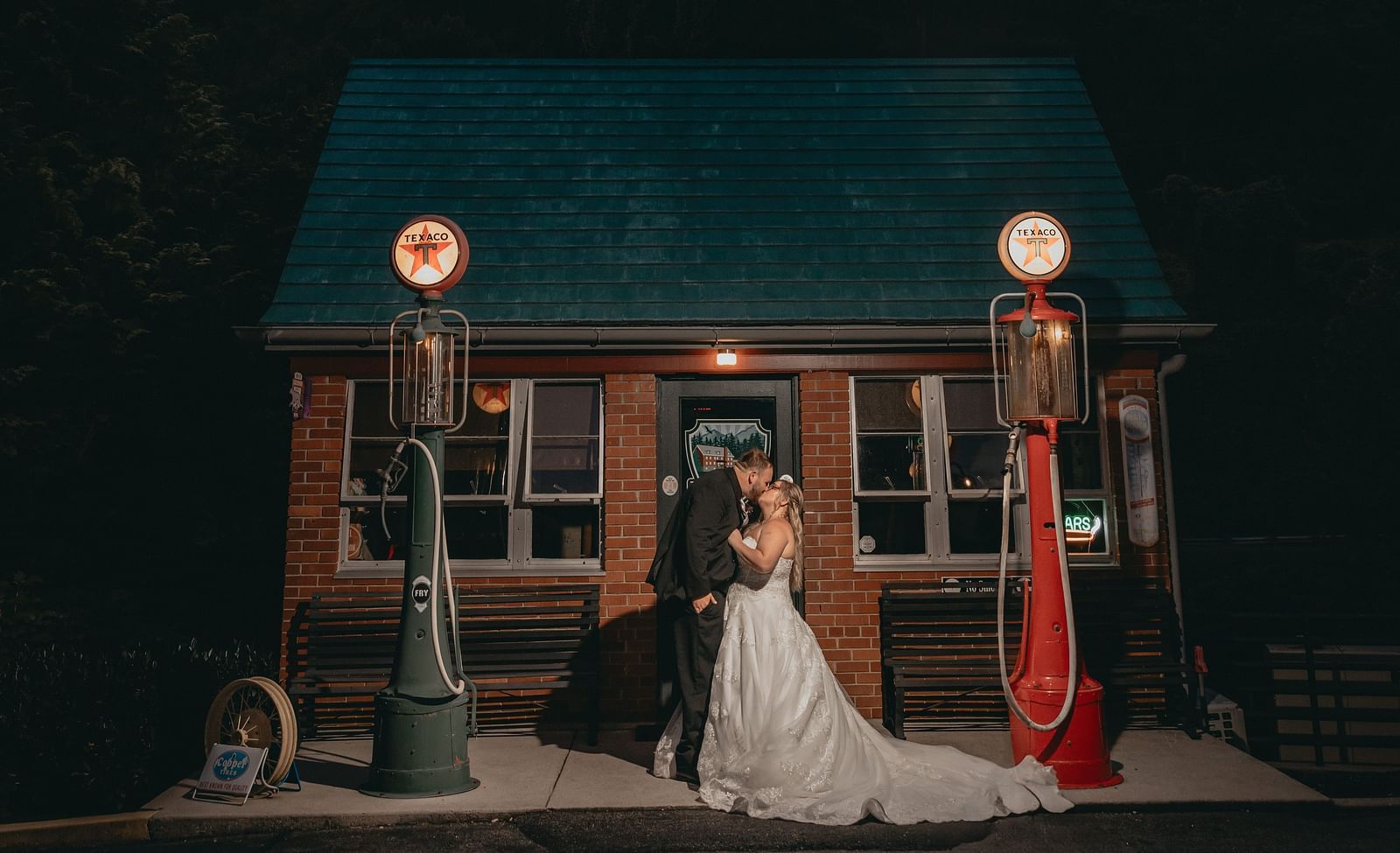 Couple in wedding attire kissing each other outside a small cottage belonging to the Historic Tapoco Lodge. The cottage has two lamp post lit on either side. 