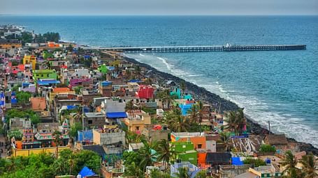 An aerial view of Pondicherry featuring colourful buildings clustered along the coastline next to the Bay of Bengal and a long pier extending into the sea.