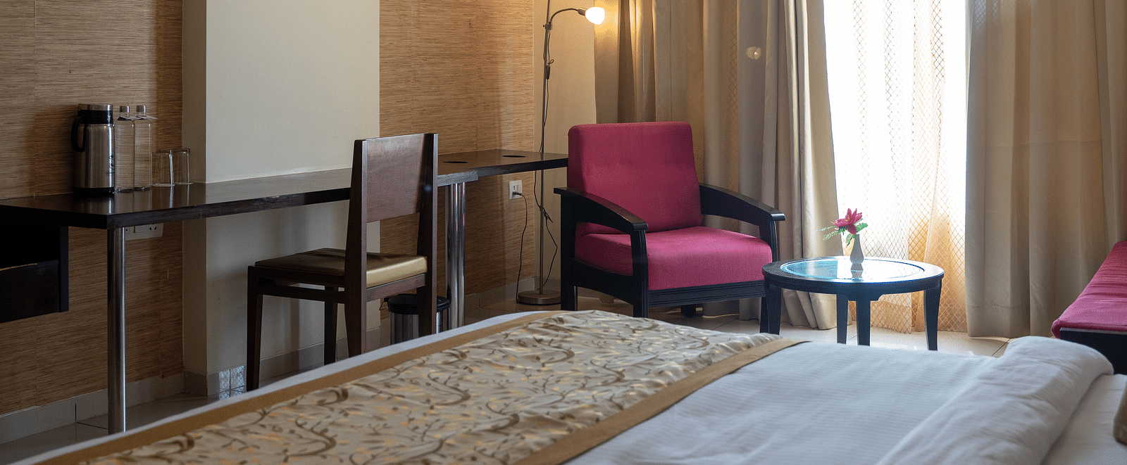 A cosy hotel room featuring a neatly made bed, an armchair, and soft lighting - Hotel Udai Median, Udaipur.