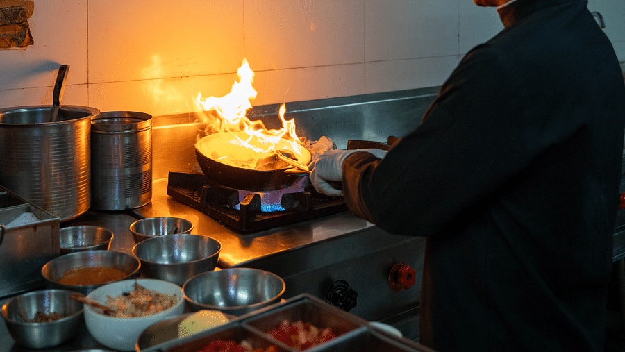 A chef preparing food in a bustling kitchen and ingredients neatly arranged can be seen on the side - Hotel Udai Median, Udaipur.