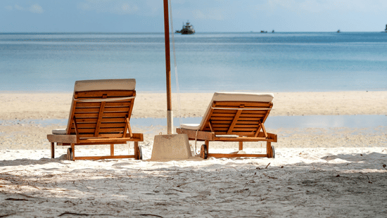image of a beach featuring two sun loungers shaded with a white umbrella