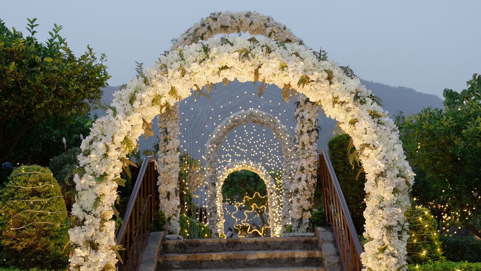 A grand floral archway leading to stairs, adorned with flowers and illuminated by soft lighting, 