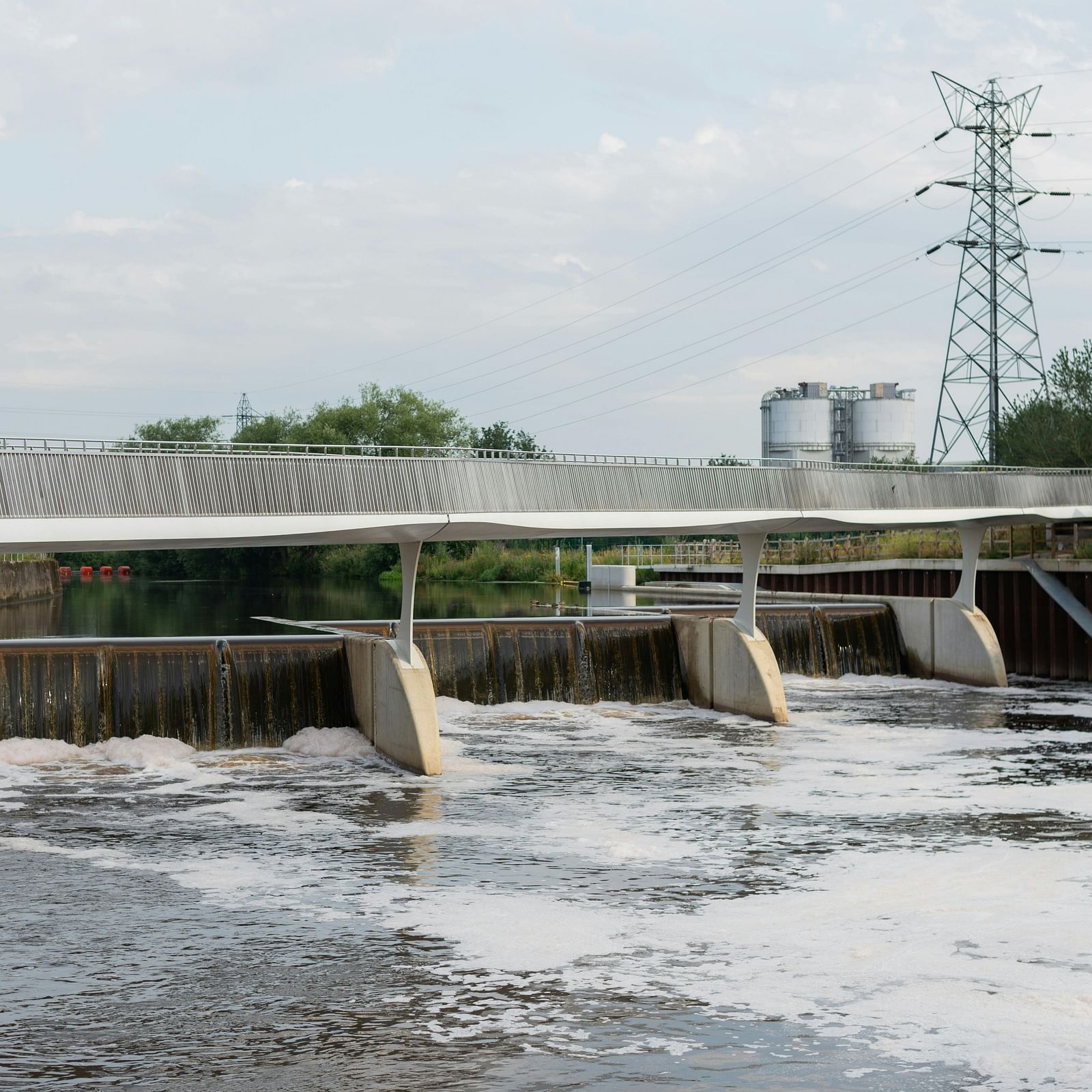A dam under a cloudy sky, featuring a modern bridge over flowing water with industrial structures in the background.