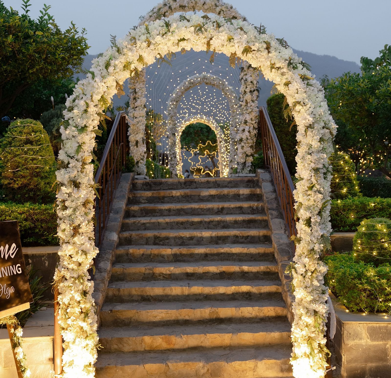 A grand floral archway leading to stairs, adorned with flowers and illuminated by soft lighting, 
