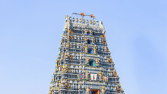 An ornate, tall South Indian temple tower stands prominently under a clear blue sky.