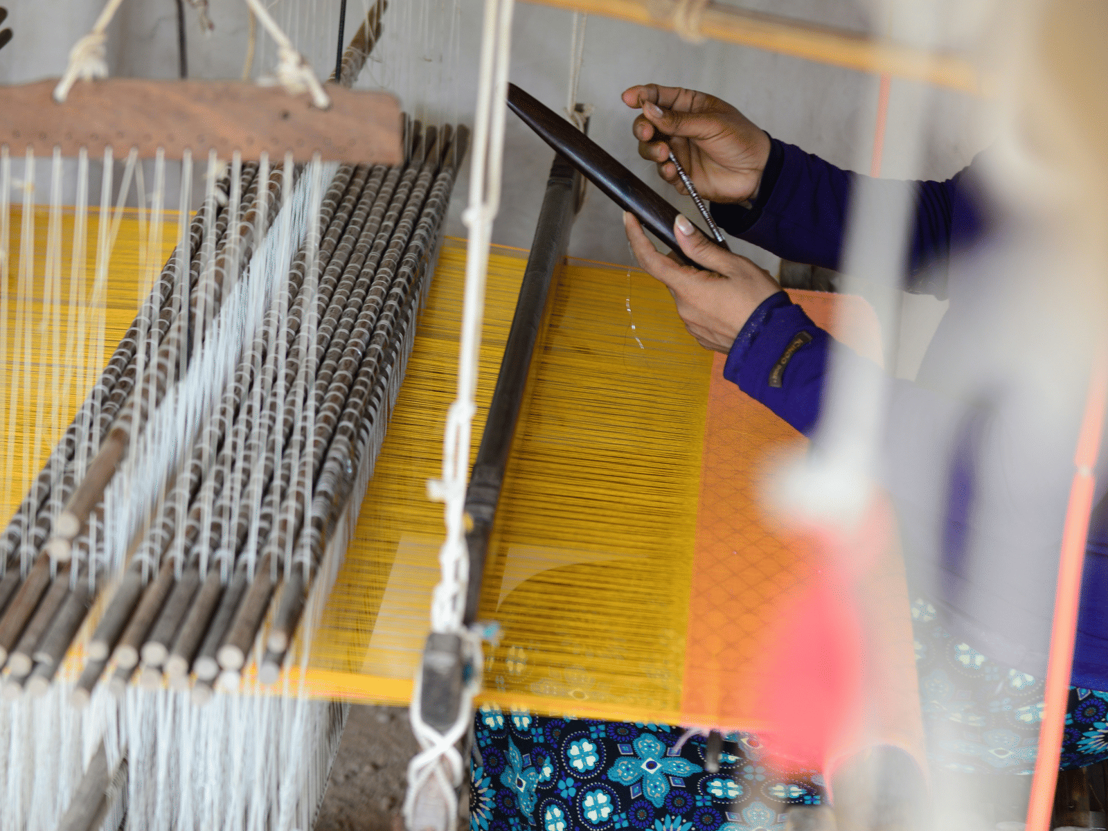 A weaver using a hand loom to weave a garment of two colours.