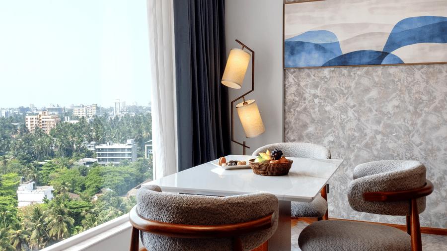 A dining area with a table, chairs, floor lamp, and large window offering panoramic views of a city landscape at Tiara by MPS.