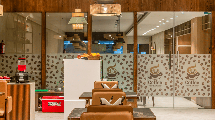 A cosy seating area at L Café featuring a wooden table set with a menu, located near a bright, modern corridor with decorative pendant lights – Skkylight Lords Inn, Nanded