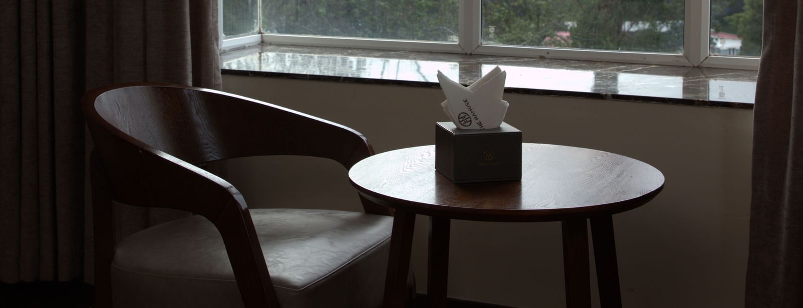 A seating area with a seater and a coffee table near a glass window at The Hamuse Hotel, Kodaikanal