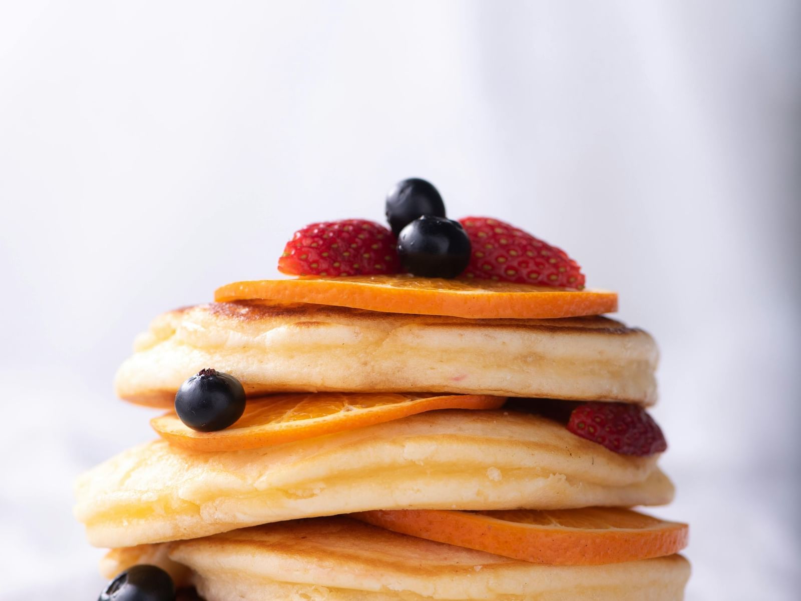 A tall stack of fluffy pancakes topped with fresh berries and fruit slices.