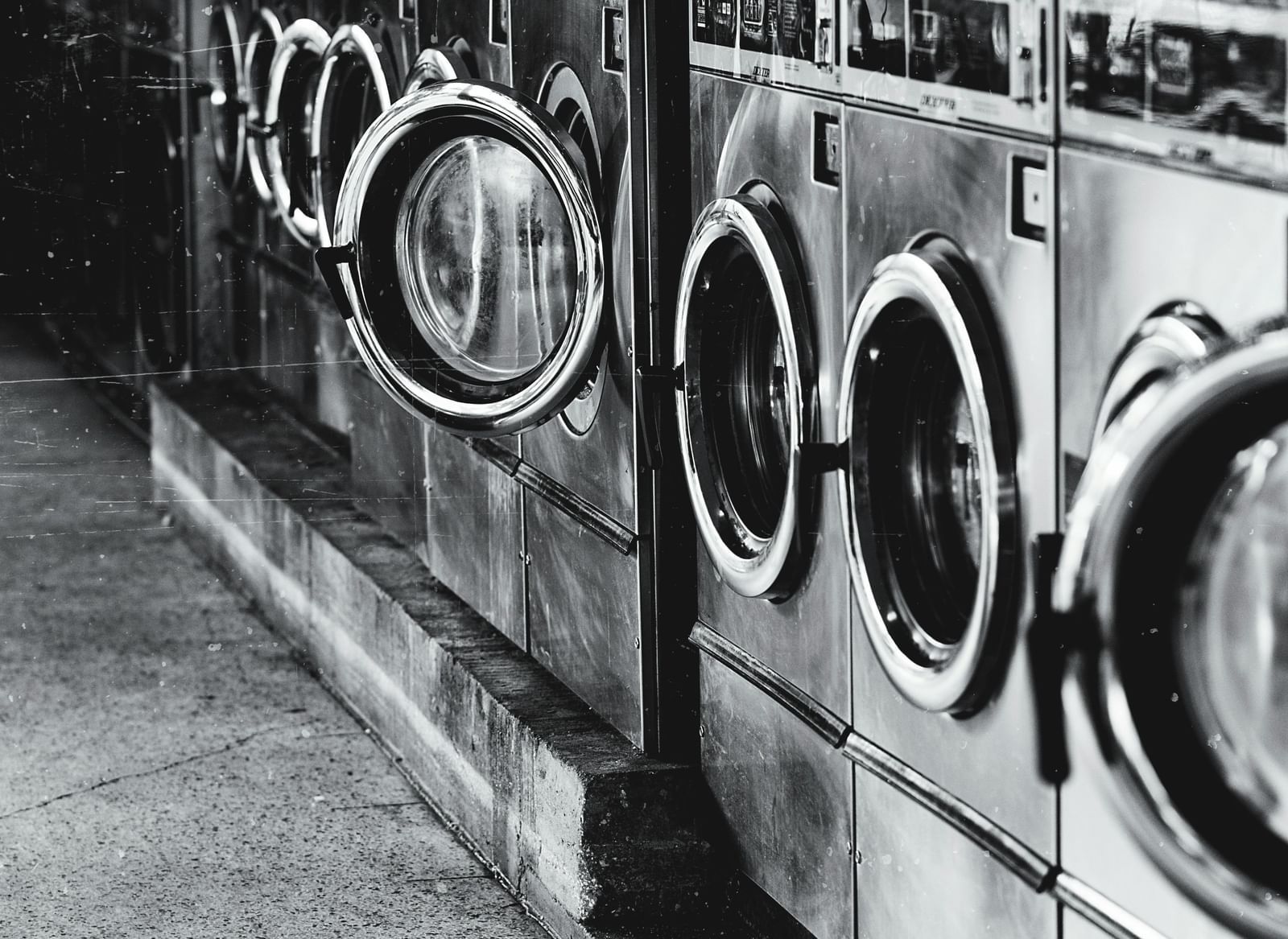 A black-and-white image of a laundromat with a row of washing machines.