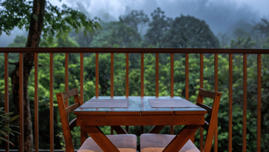 An outdoor table and chairs are set on a balcony with a view of a misty forest.