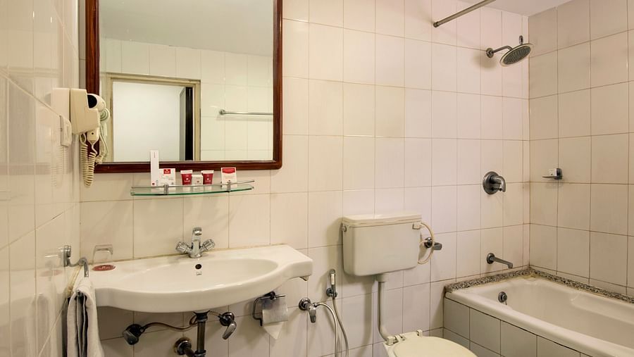 A hotel bathroom with a sink, toilet, and a dark rug on the tiled floor - Lords Eco Inn Dahej
